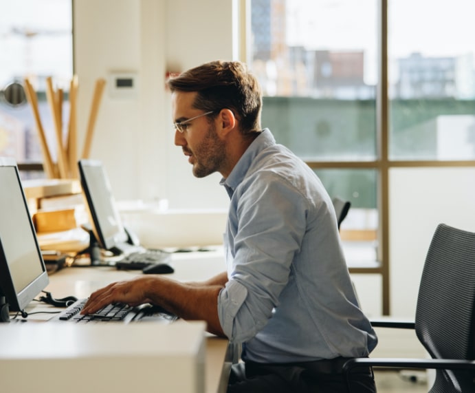 An office worker at a desktop computer in a bright open-plan office