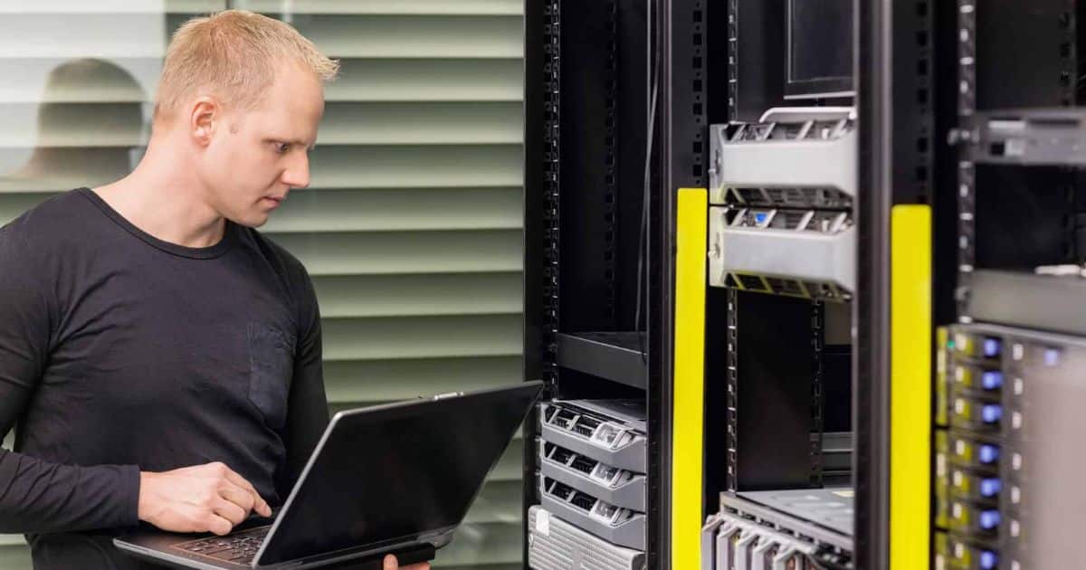 A technician with a laptop working beside server racks in a data centre