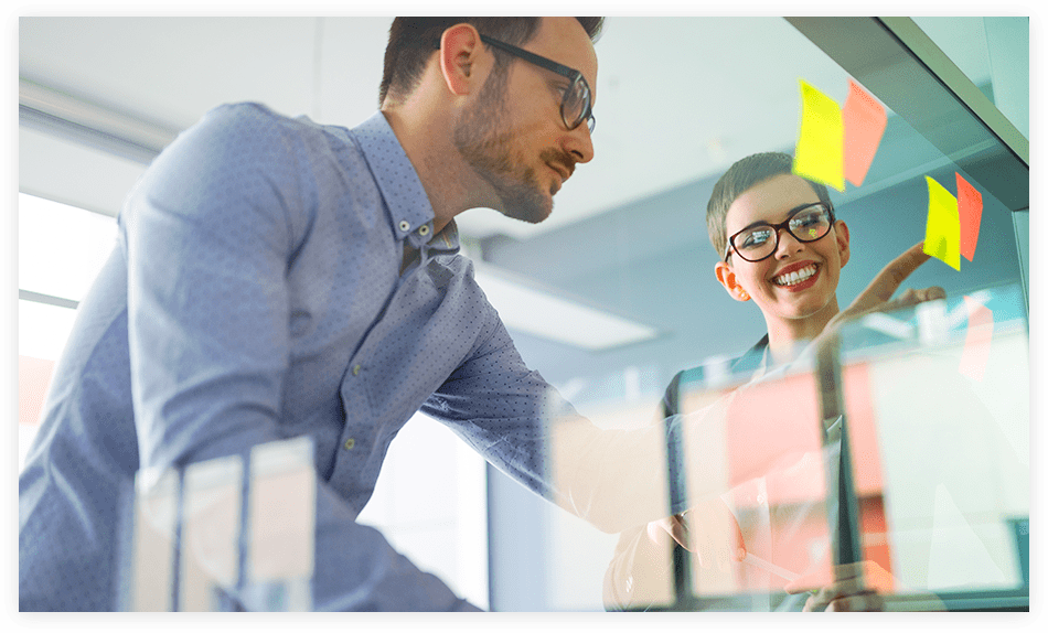 Two colleagues planning with sticky notes on a glass office wall