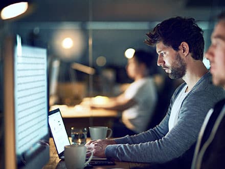 A man reviewing data on a desktop screen in a dimly lit office