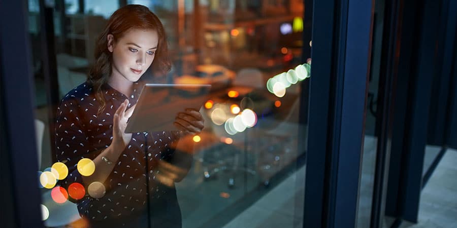 A woman using a tablet beside an office window at night, city lights behind her
